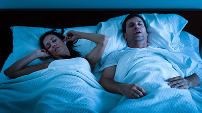 Woman plugging ears inbed next to snoring man
