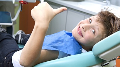 Smiling little boy in dental chair giving thumbs up