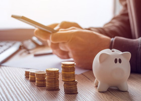 Man using a calculator with a piggy bank and coin stacks nearby