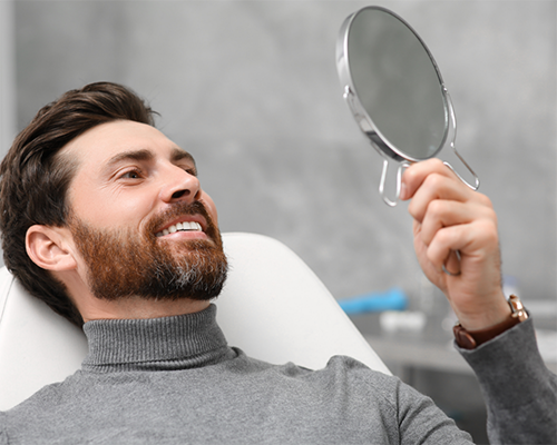 Bearded man admiring his smile in a mirror at the dental office