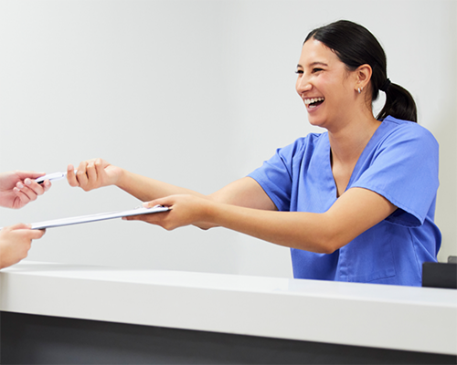 Smiling dental team member handing clipboard to patient