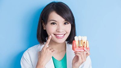 Irving implant dentist points to her smile and holds model of dental implants