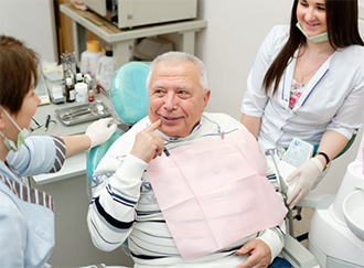 Senior man in the dental chair pointing at his mouth