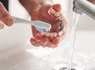 Cleaning a denture with a toothbrush in a sink