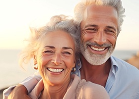 Older couple smiling on the beach with their dentures