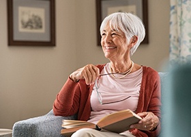 Senior woman in chair holding glasses and book