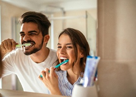 Couple smiling while brushing their teeth