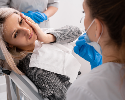 Woman holding her cheek in pain while seeing her dentist