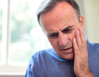 Man in blue shirt with hand on cheek due to dental pain