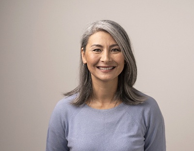 Woman with greying hair wearing grey shirt while smiling
