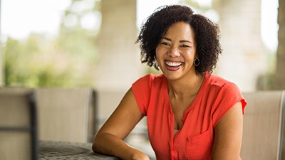 Woman in red shirt smiling with dental implants in Irving while outside