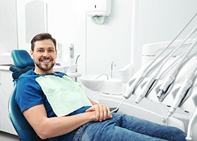 Man in blue shirt and jeans smiling in dental chair