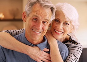 Older couple smiling with woman’s arms around man 