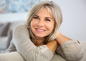 Older woman in grey shirt smiling with elbows on couch