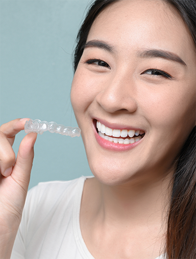 Young woman holding a clear aligner near her smile