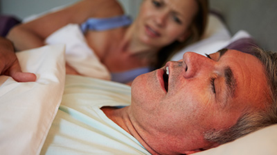 Frustrated woman in bed next to snoring man