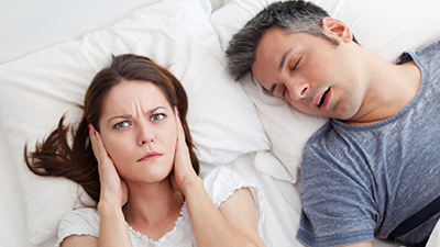 Woman covering ears next to snoring man