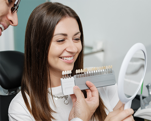 Young woman looking in a mirror while a dentist holds veneers by her smile