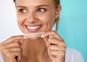 woman smiling with whitening strip in hand 