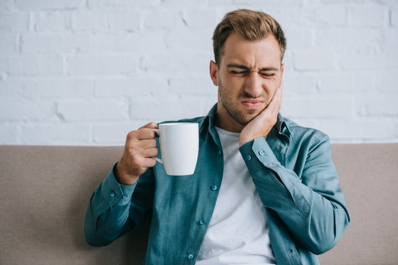 Man with coffee mug rubbing jaw due to pain