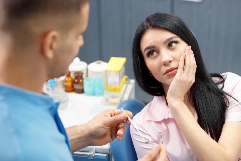 Patient holding their cheek where their dental bridges are coming loose