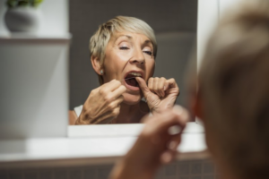 Woman flossing her teeth in bathroom mirror
